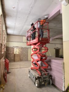 Photo of the inside of Gateway Lodge. Workers are on a telescopic platform working to apply mesh to the ceiling prior to replastering.
